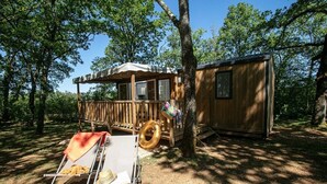 Een houten hut met een terras, een lounge stoel en een barbecue.