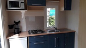 Une cuisine de taille réduite équipée d’un four à micro-ondes, d’une cuisinière, d’un évier et de meubles de rangement bleu foncé.
