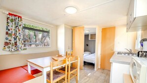 Une pièce compacte comprenant un coin cuisine, un espace repas avec une table et des chaises, un lit dans la pièce adjacente et une fenêtre avec des rideaux.