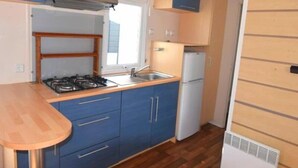 A compact kitchen with blue cabinets, a gas stove, a sink, and a white refrigerator. - ZEcamping 3* piscine chauffée dog friendly sauna locatif 28m2 4 pers (Huelgoat)
