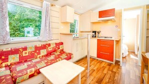 Espaço compacto com sofá, uma mesa pequena, cozinha compacta e janela com cortinas.