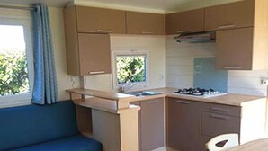 A compact kitchen with a dining area, a sofa, and a window with curtains. - ZEcamping 3* piscine chauffée mobil-home 36m2 6 pers (Huelgoat)