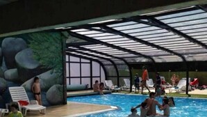 An indoor swimming pool with clear water, surrounded by lounge chairs and a covered area with a view of the outdoors. - ZEcamping 3* piscine chauffée mobil-home 36m2 6 pers (Huelgoat)