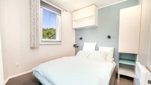 Una camera da letto con un letto, una finestra con tende, un armadio a muro e un termosifone.