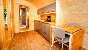 Een compact houten vakantiehuisje met een kitchenette, een eethoek en een douchecabine met glazen wanden.