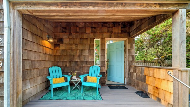 Una terraza de madera con dos sillas Adirondack turquesas y una pequeña mesa, una puerta de madera y un muro de madera.