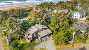 Vista aérea de una zona residencial costera con casas rodeadas de árboles frondosos, una playa y vistas al océano.