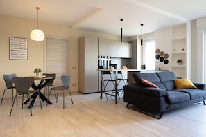A modern living room with a sofa, dining table, chairs, and a kitchen area.