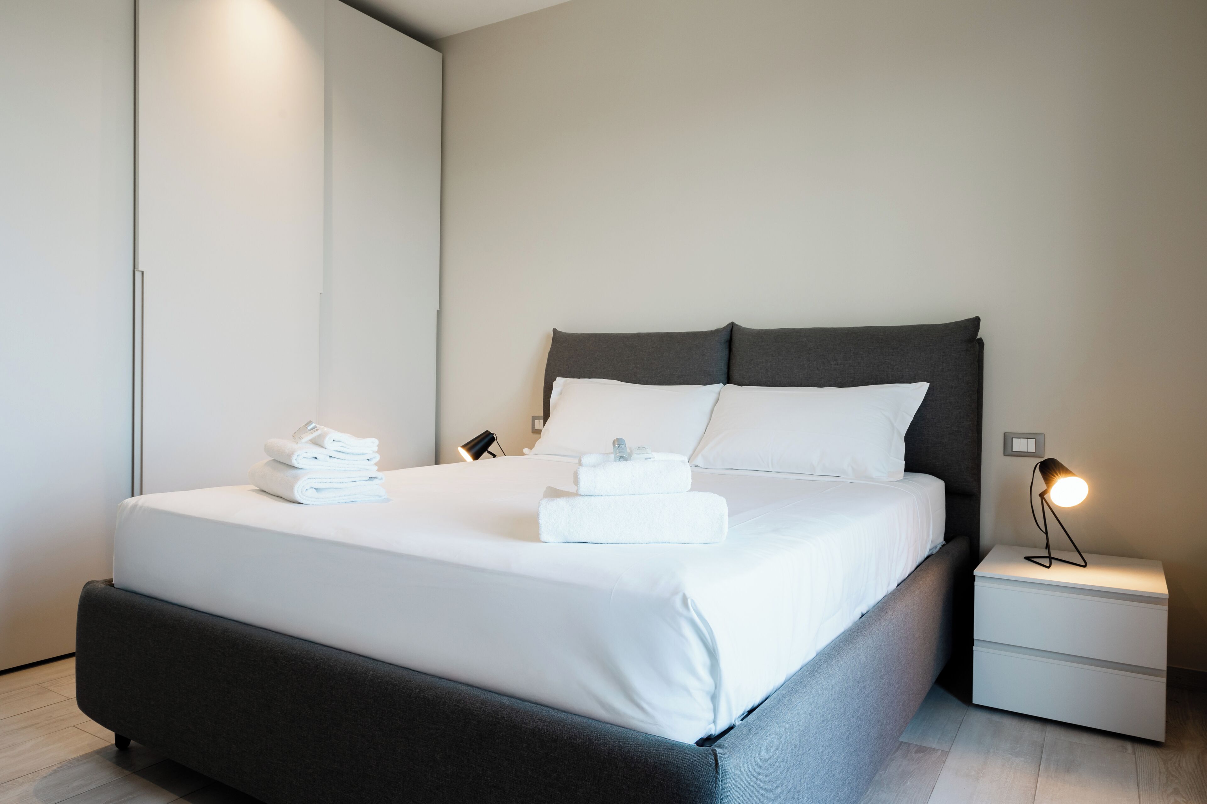 A modern hotel room with a large bed, a bedside table with a lamp, and neatly folded towels on the bed.
