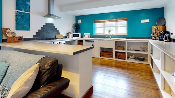 Una cocina moderna con una isla central, un área de comedor con sofá y vistas al exterior.
