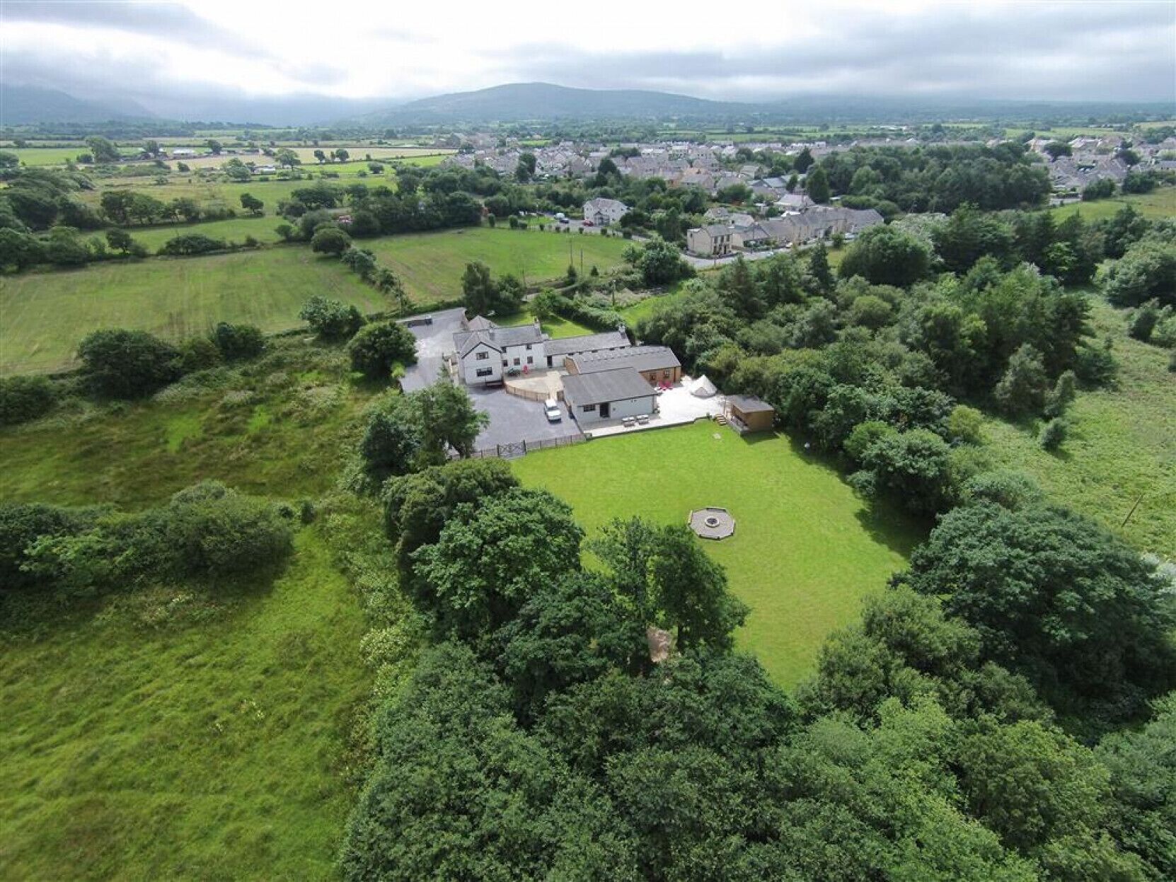 Luchtbeeld van een landelijk gebied met een groot huis, omgeven door weelderige begroeiing en velden.