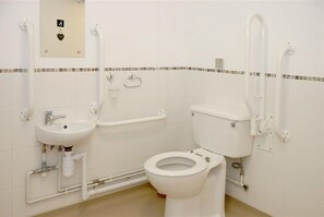A small, white bathroom with a toilet, sink, and grab bars.