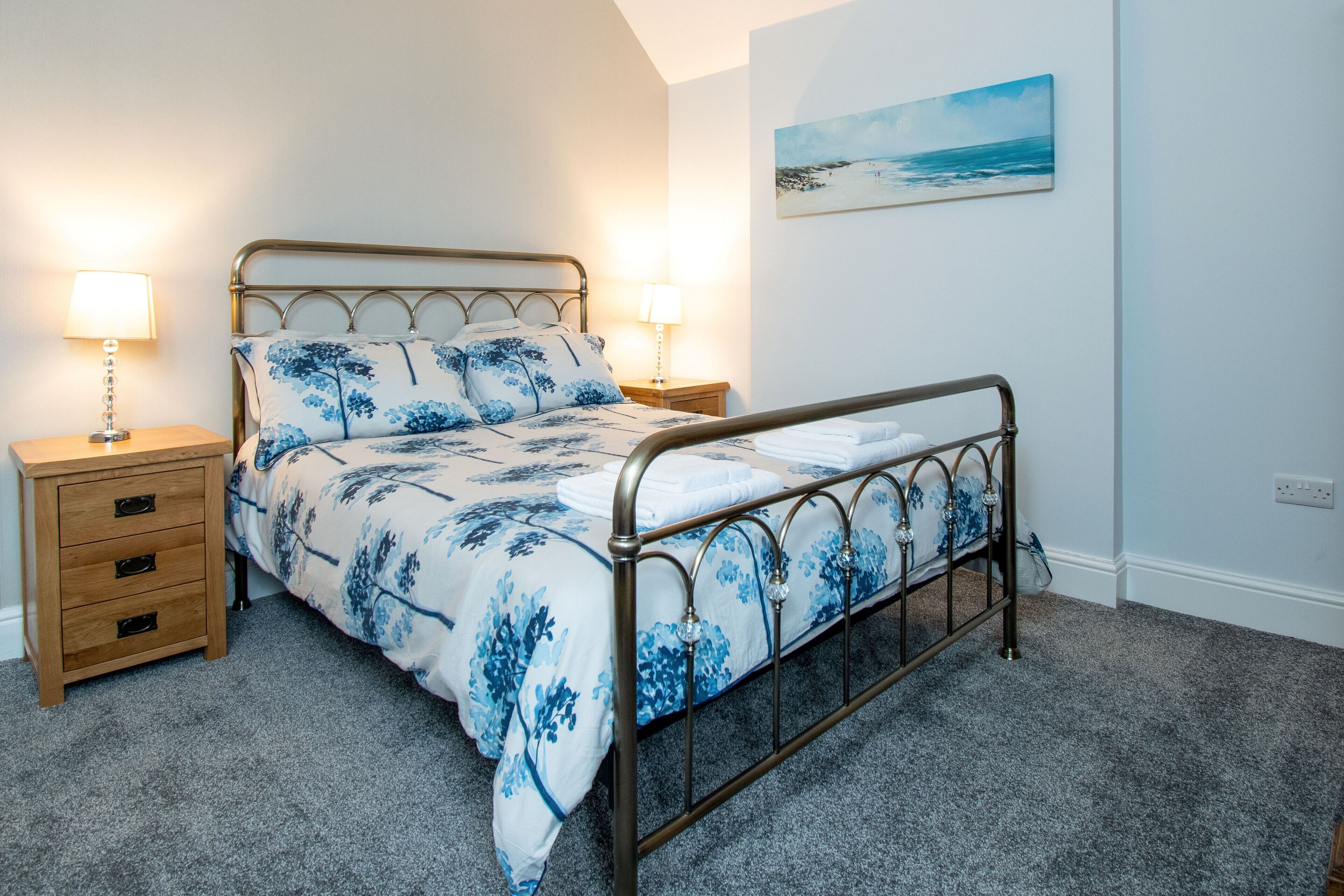 A bedroom with a bed, two bedside tables, and a wall-mounted painting.