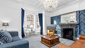 Ein Wohnzimmer mit blauem, gemustertem Wandpapier, einem Kamin, einem Fernseher und einer Chandelier.