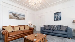 Ein Wohnzimmer mit braunem Ledersofa, einem blauen Sofa, einem Holztisch und zwei Bildern an den Wänden.