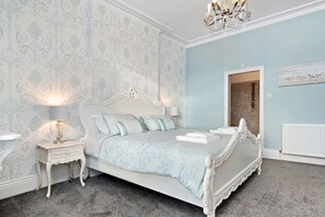 Ein Schlafzimmer mit einem großen Bett, einem Nachttisch, einer Lampe und einem Kronleuchter.