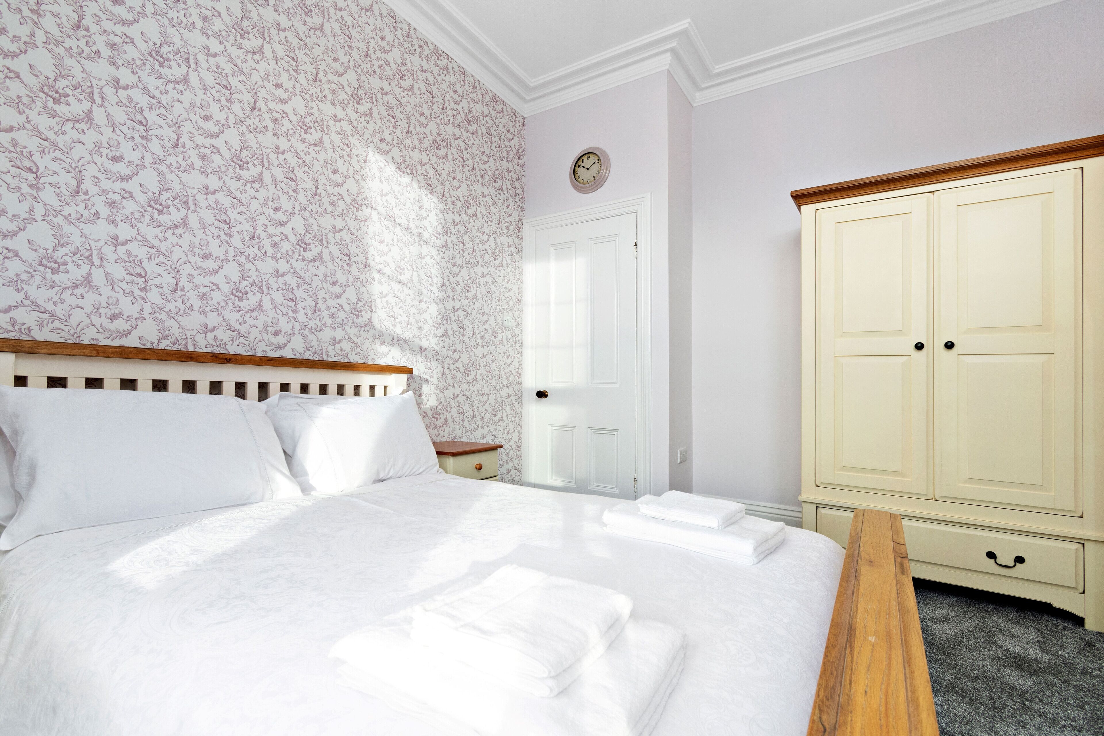 Une chambre à coucher bien rangée, avec un grand lit, un banc en bois, une armoire et une horloge au mur.