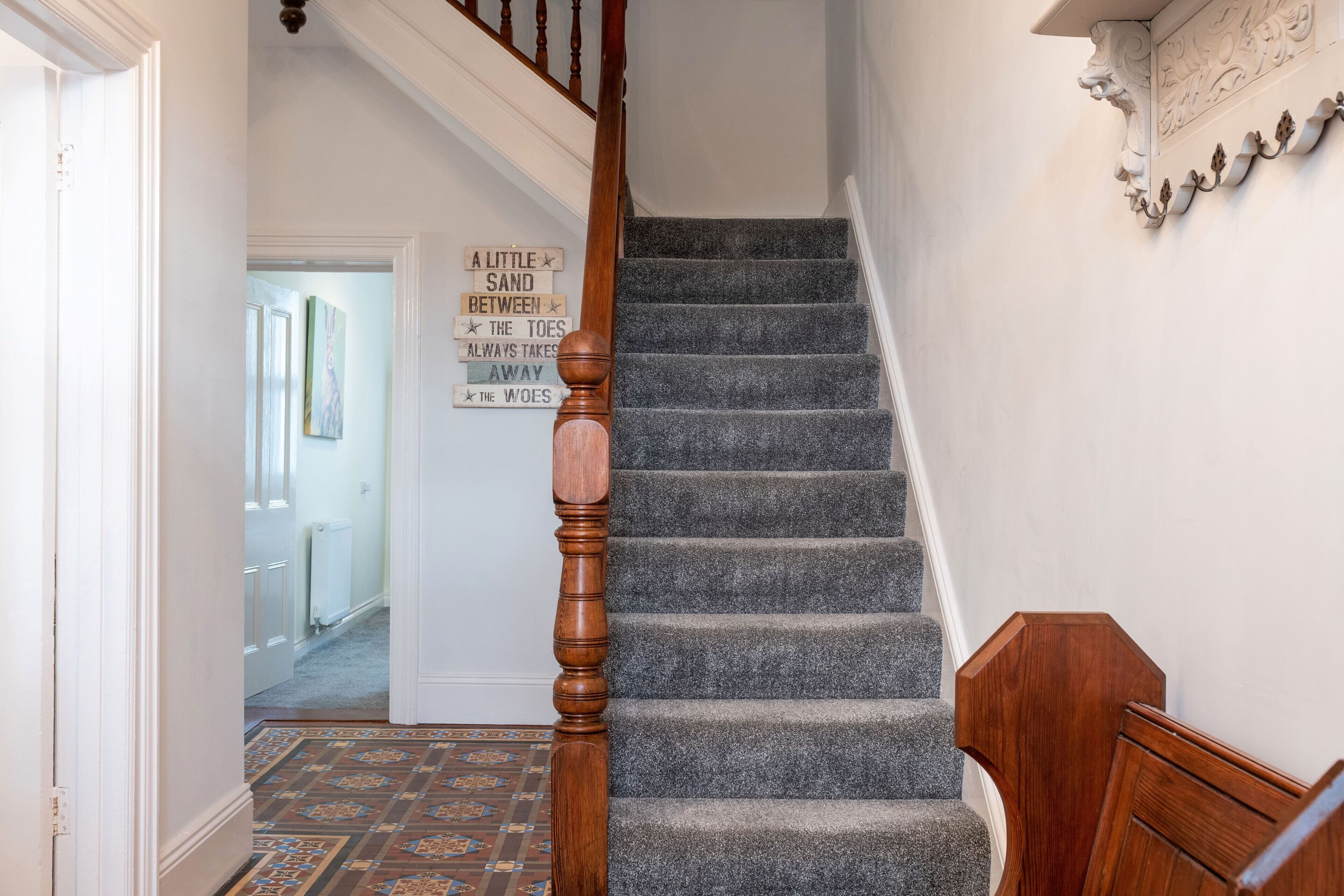 A staircase with a wooden handrail and carpeted steps. A sign with a quote is visible on the wall.