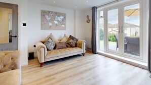 Een ruime woonkamer met een groot raam, een beige bank met opvallende kussens, en een wereldkaart aan de muur.