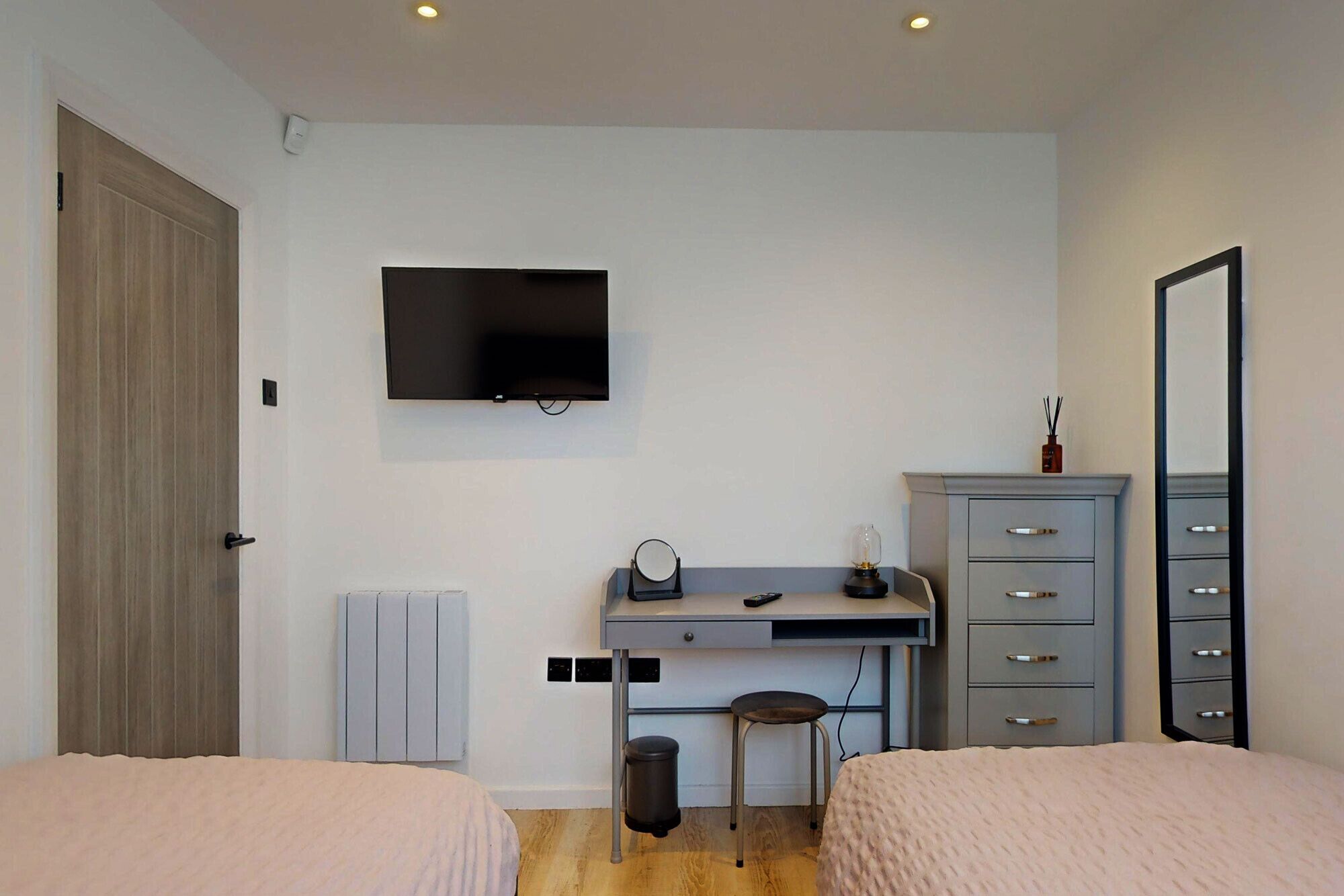 Une chambre avec deux lits, un bureau avec une chaise, une télévision, une commode et un miroir.