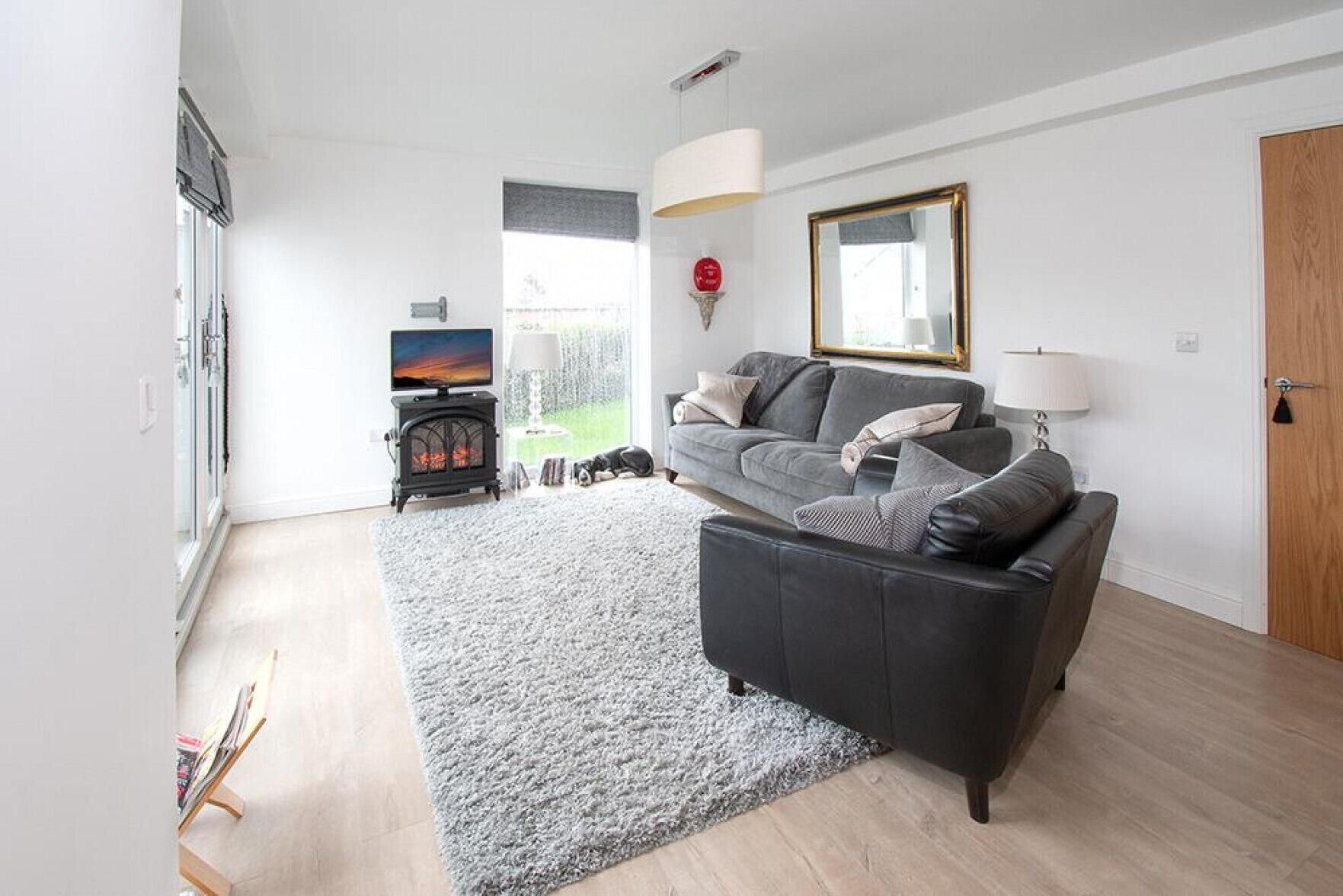 A modern living room with a grey sofa, a fireplace, a TV, and a large window.