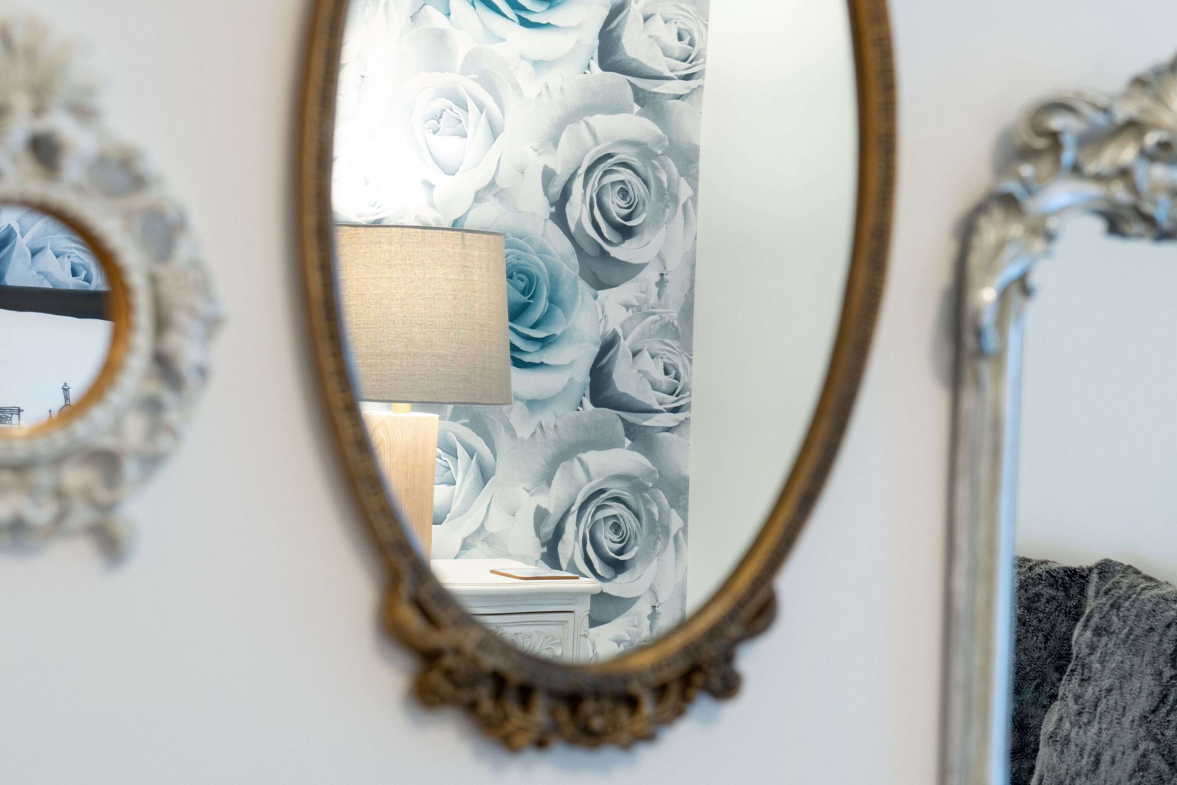 Ein Zimmer mit Spiegel, der eine Wand mit floralem Tapetenmuster reflektiert.