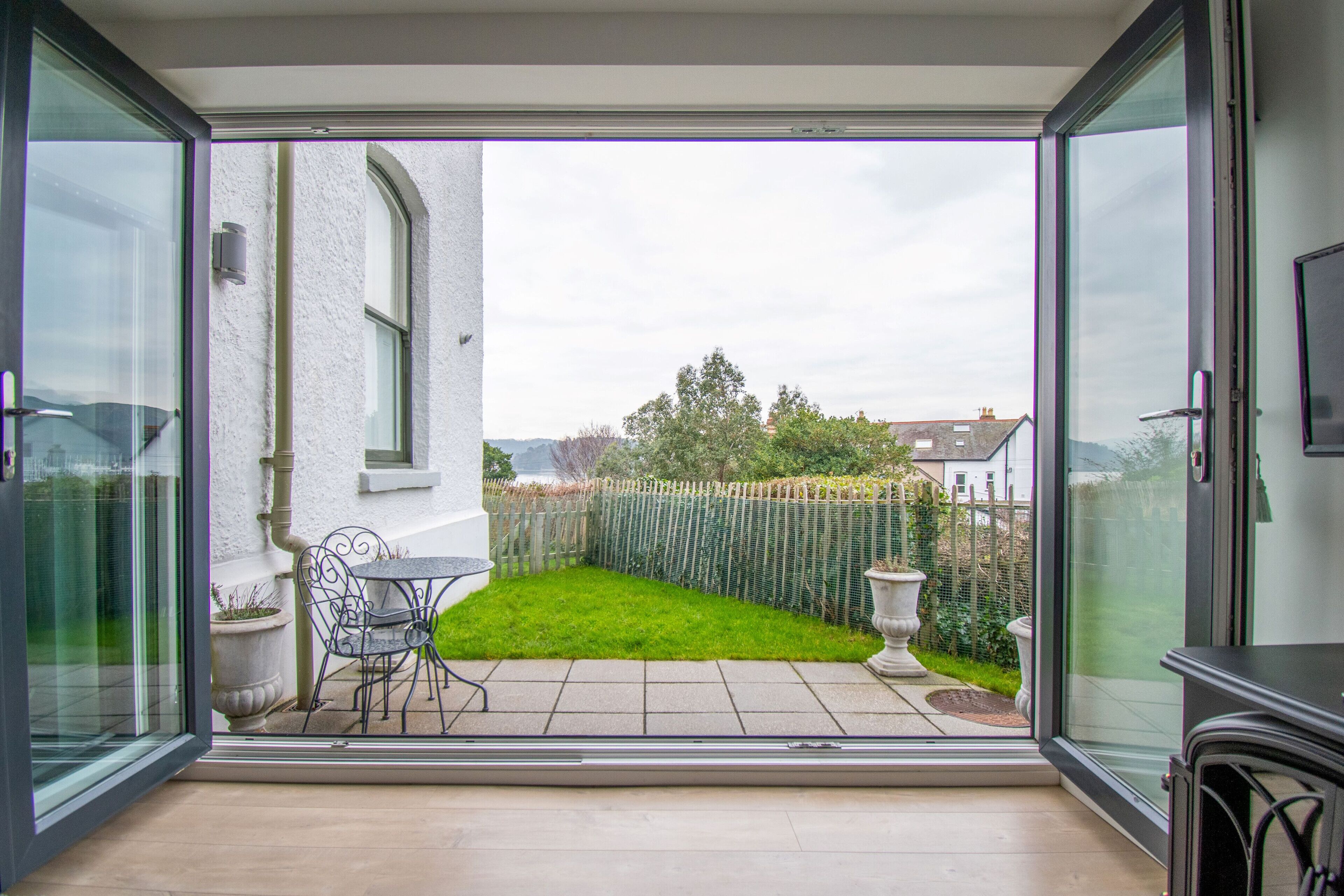 A conservatory with a glass door, a small patio area with a table and chairs, and a view of a fenced garden.