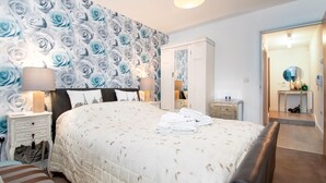 A bedroom with a large bed, a nightstand with a lamp, a dresser, and a mirror. - Eleven - One Bedroom Cottage, Sleeps 2 (Deganwy)
