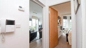 A modern interior with a white wall-mounted phone, a wooden door leading to a living area with a sofa and a TV, and a hallway with a carpeted floor. - Eleven - One Bedroom Cottage, Sleeps 2 (Deganwy)