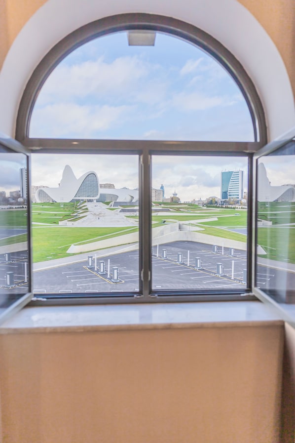 A view through a window with a curved top, displaying a modern building with a unique design, a parking area, and a grassy field. - The Central Point Hotel Baku (Baku)