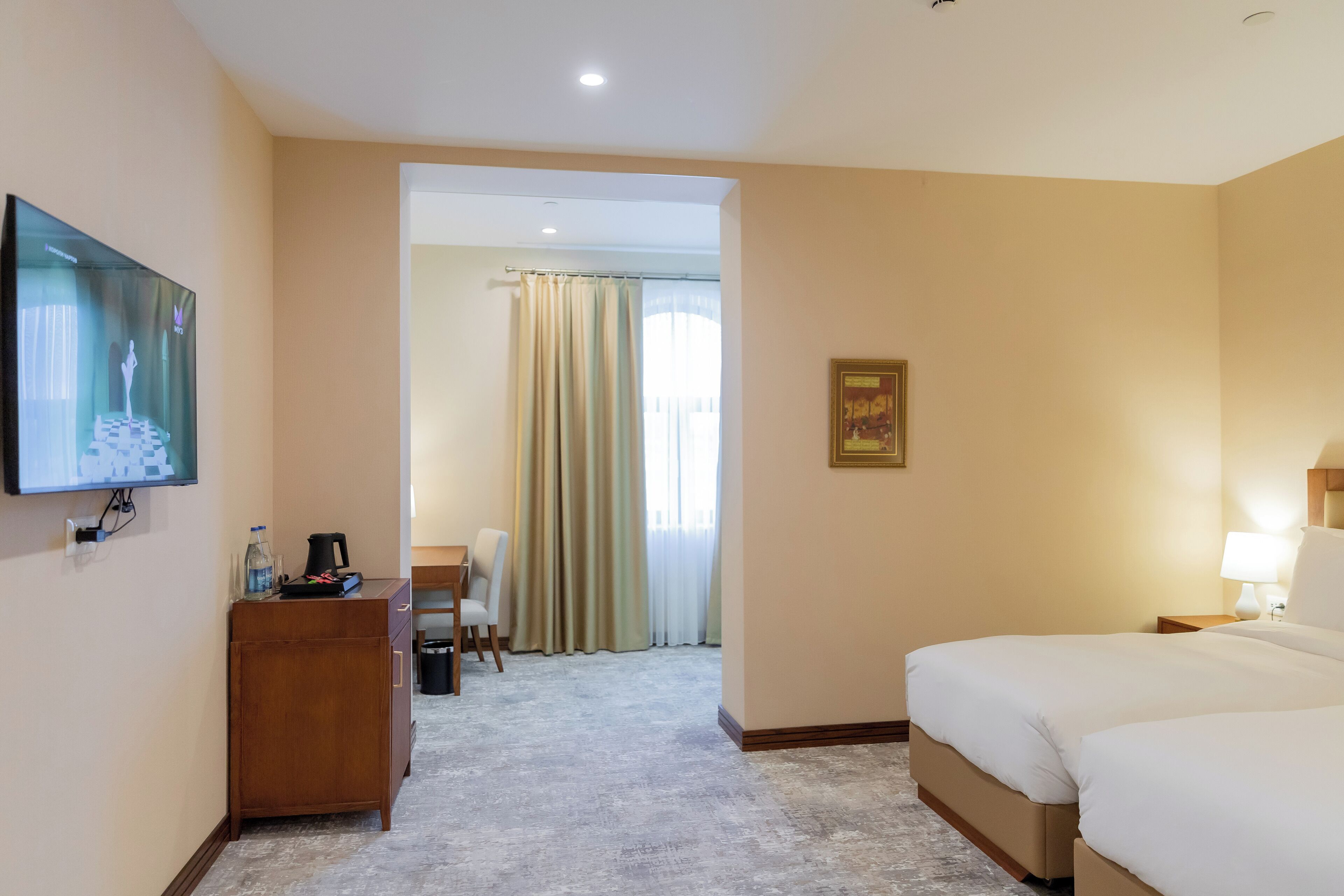 Ein Hotelzimmer mit einem Bett, einem Schreibtisch mit Stuhl, einem Fernseher und einem Fenster mit Vorhängen.