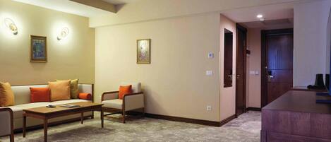 Une chambre d’hôtel avec un canapé, des fauteuils, une petite table et un meuble en bois.