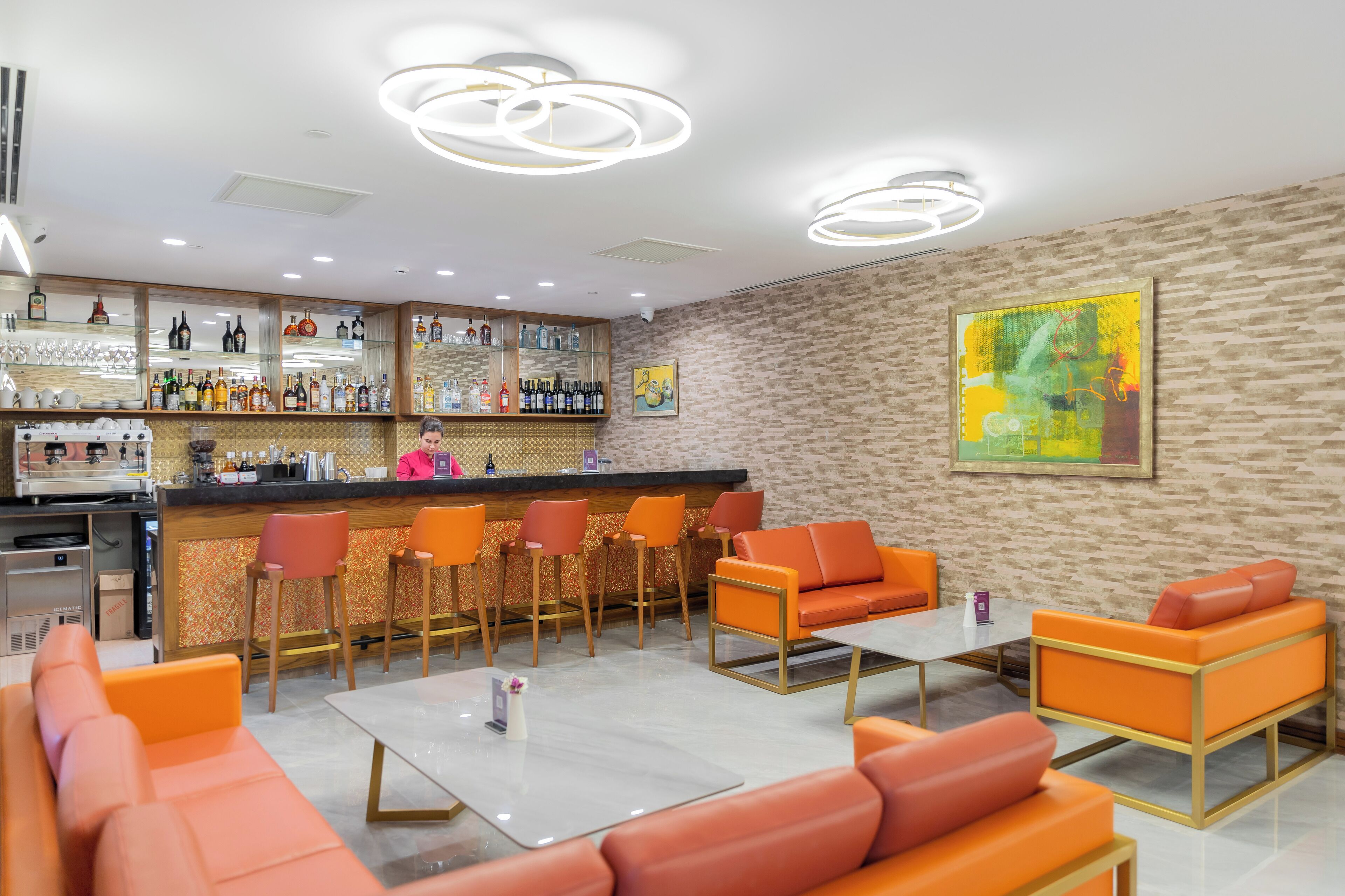 Een moderne bar met een barman, oranje zitplaatsen en diverse drankflessen.