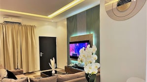 Ein modernes Wohnzimmer mit einer Couch, einem Couchtisch und einem Fernseher. Eine Tür und ein Fenster mit Vorhängen sind vorhanden.