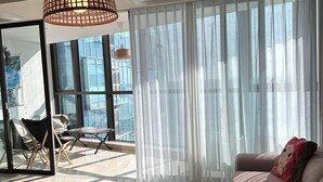 A modern living room with a glass coffee table, a sofa, and sheer curtains.