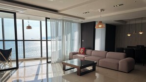 A modern living room with a large window, a sofa, a coffee table, and a dining area with chairs and a laptop.