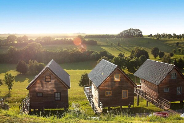 Tres cabañas de madera con vista a un campo verde y árboles al fondo.