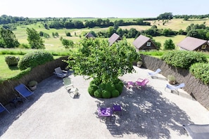 Eine Terrasse mit einem großen Baum, mehreren Stühlen und Blick auf die Landschaft.