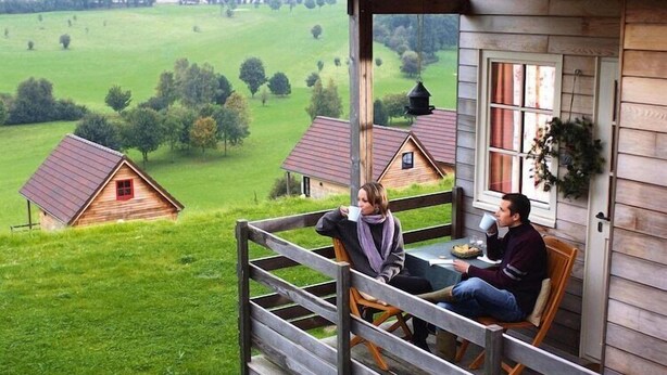 A wooden cabin with a porch overlooking a green landscape.