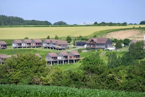 Eine Reihe von Holzhäuschen mit Balkonen, eingebettet in eine üppige grüne Landschaft unter blauem Himmel.