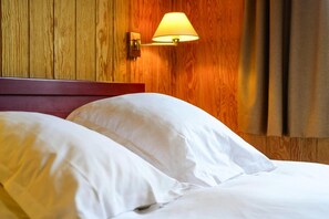 Ein Hotelzimmer mit einem hölzernen Kopfteil, zwei weißen Kissen und einer Wandlampe.