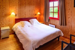 A wooden-paneled room with a bed, two bedside lamps, and a window with curtains. - Wooden Chalet in Abbeville near Somme Bay (Grand-Laviers)
