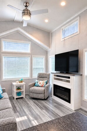 A living room with a ceiling fan, a fireplace, a television, and a window with blinds.