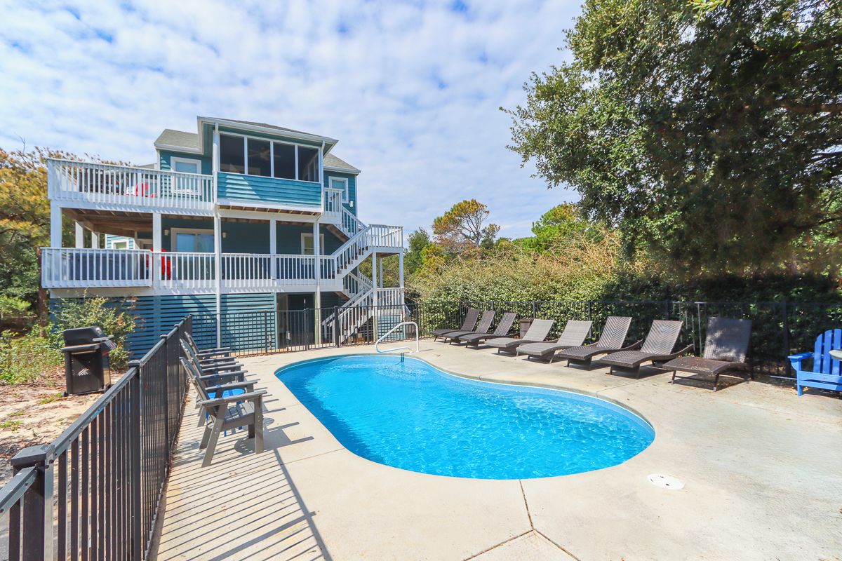 A two-story building with a swimming pool, deck chairs, and a fenced area.