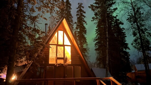 A cabin with a triangular roof, a large window, and a wooden deck. - Jupiter Peaks Hideaway (Anchorage)
