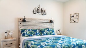 Une chambre à coucher avec une tête de lit en bois, une literie à motifs floraux, une table de chevet avec des tiroirs et des œuvres d’art murales.