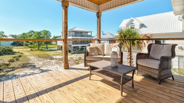 Une terrasse extérieure couverte, aménagée avec des meubles en osier et une table, d’où l’on a vue sur une plage et des immeubles d’habitation.