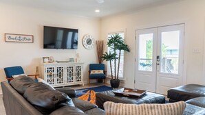 Un salon avec un canapé en cuir, un fauteuil bleu, une armoire blanche, un téléviseur, une horloge et une plante en pot.
