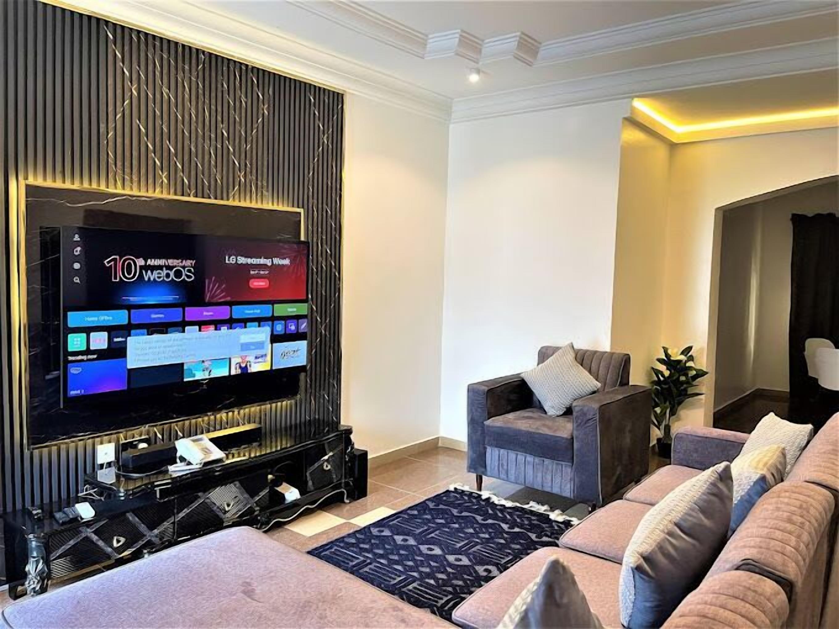 A modern living room with a large flat-screen TV, a grey sofa, and a patterned rug.