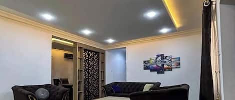A modern living room with two black sofas, a coffee table, and recessed ceiling lighting.